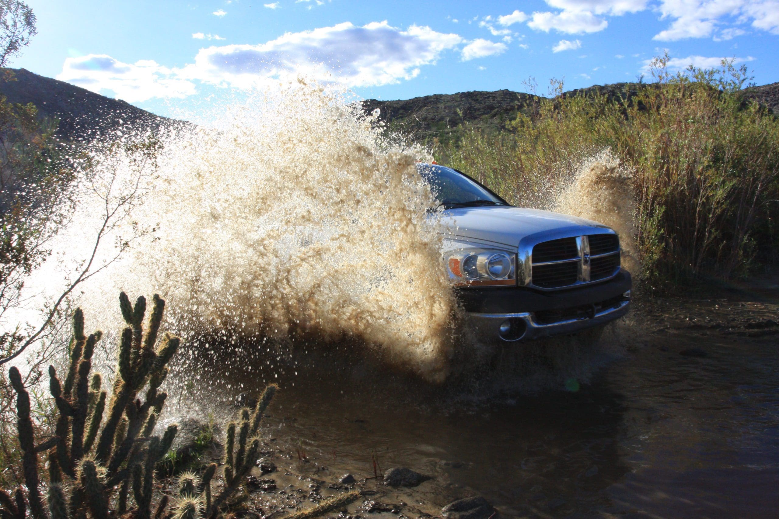 White Dodge Ram truck splashing through a shallow river while off-roading through California coastal sage and chaparral